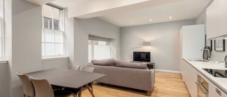 A modern apartment with a dining area, sofa, TV, and kitchen.