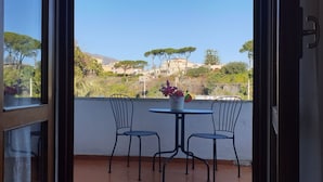 A balcony with two chairs and a table, overlooking a hillside with buildings and trees. - Il Giardino di Villa Anna (Trecase)