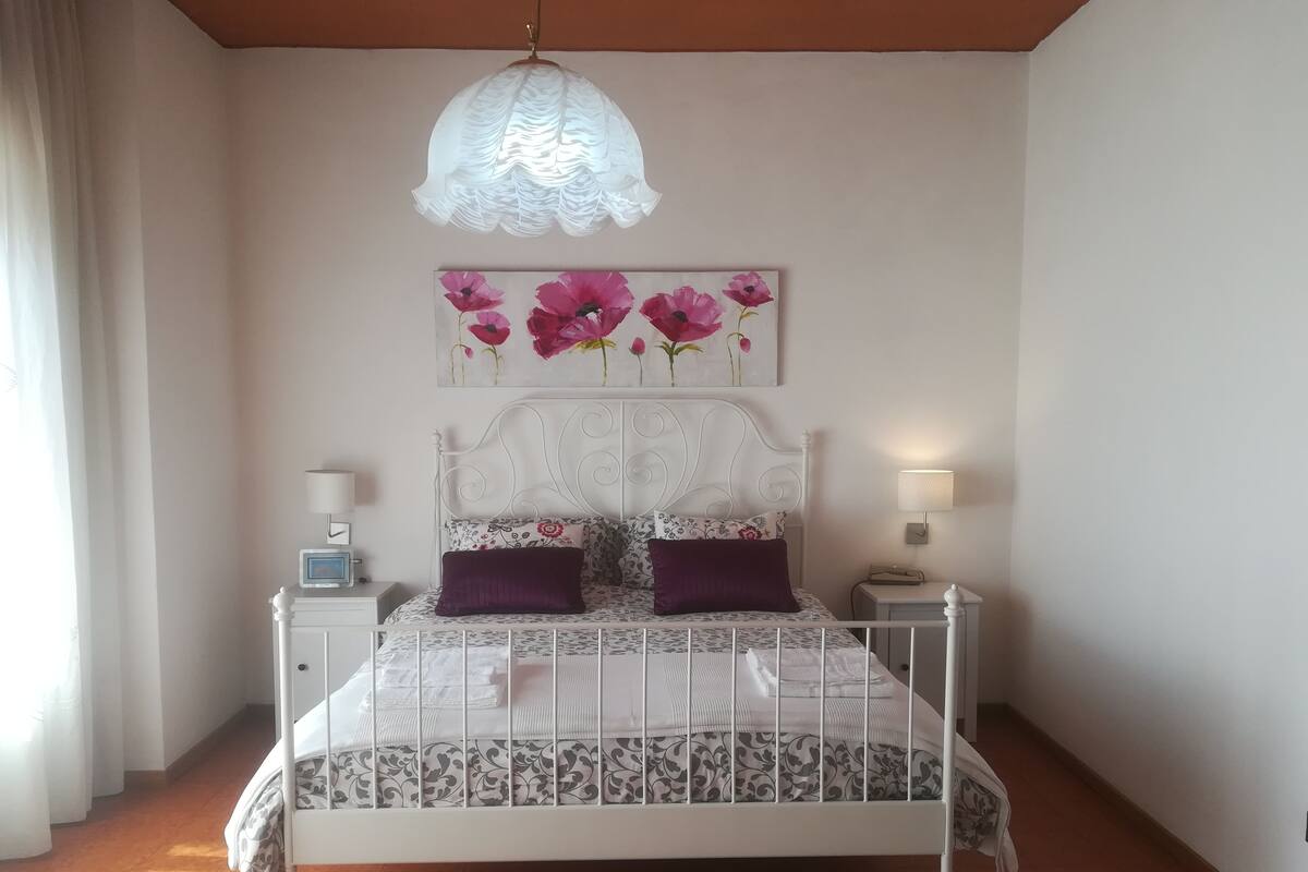 Un dormitori ordenat amb un llit, dues taules de nit, una làmpada penjada a la paret i una llum al sostre.