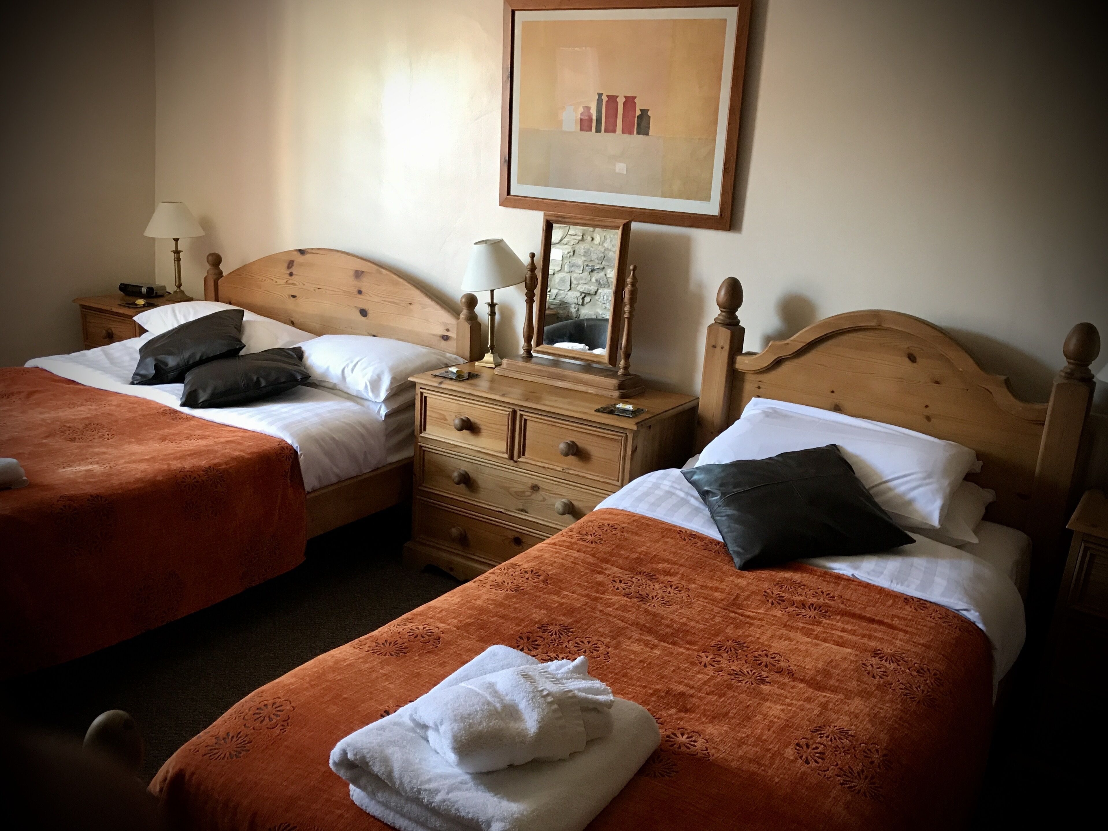 A hotel room with two beds, each with a wooden headboard, a nightstand with a lamp, and a dresser with a mirror.