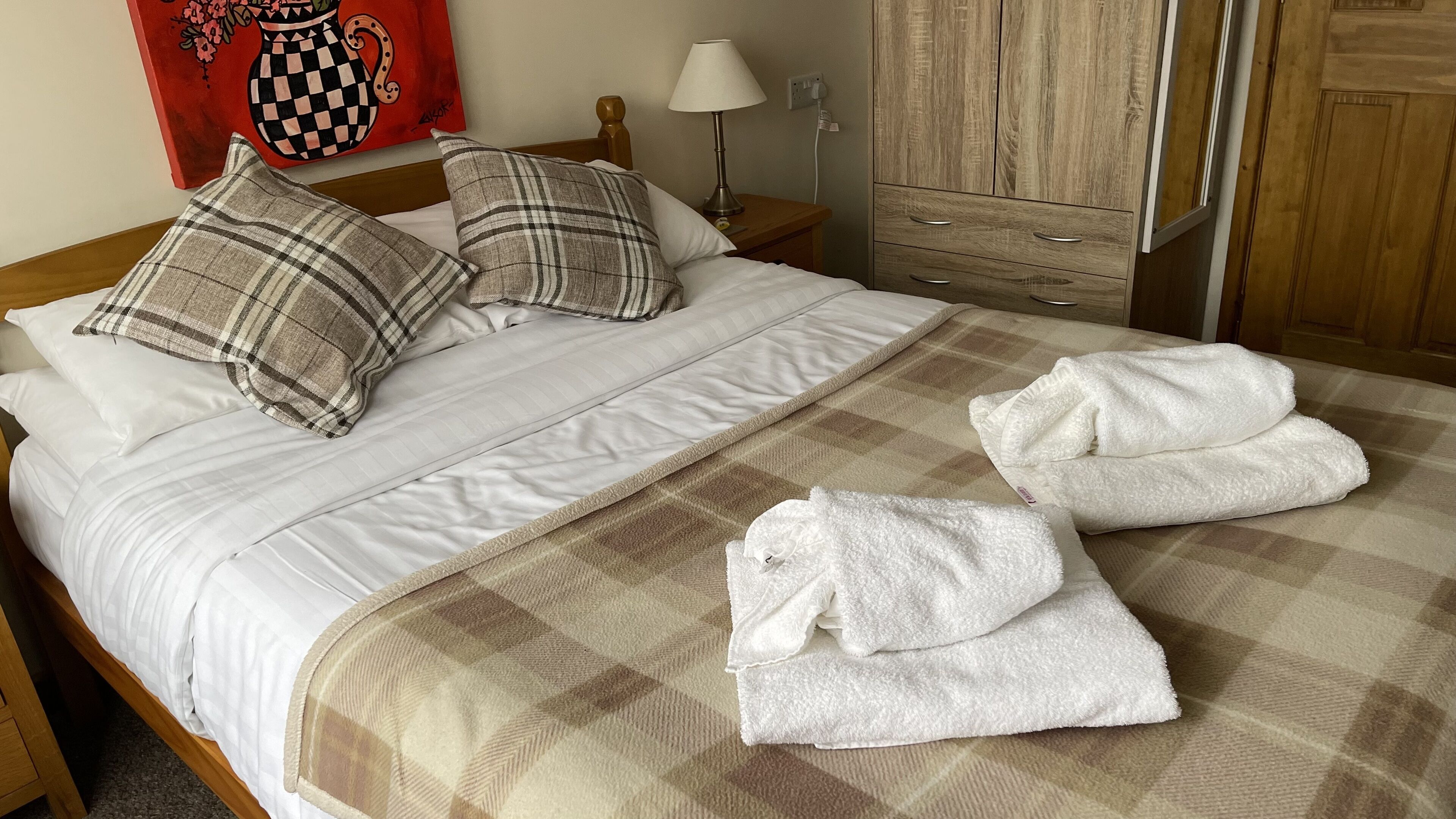A neatly made bed with plaid pillows, a checkered blanket, and two folded towels on a checkered bedspread.