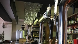 Zona de bar con múltiples grifos, una barra de madera y una lámpara de araña.