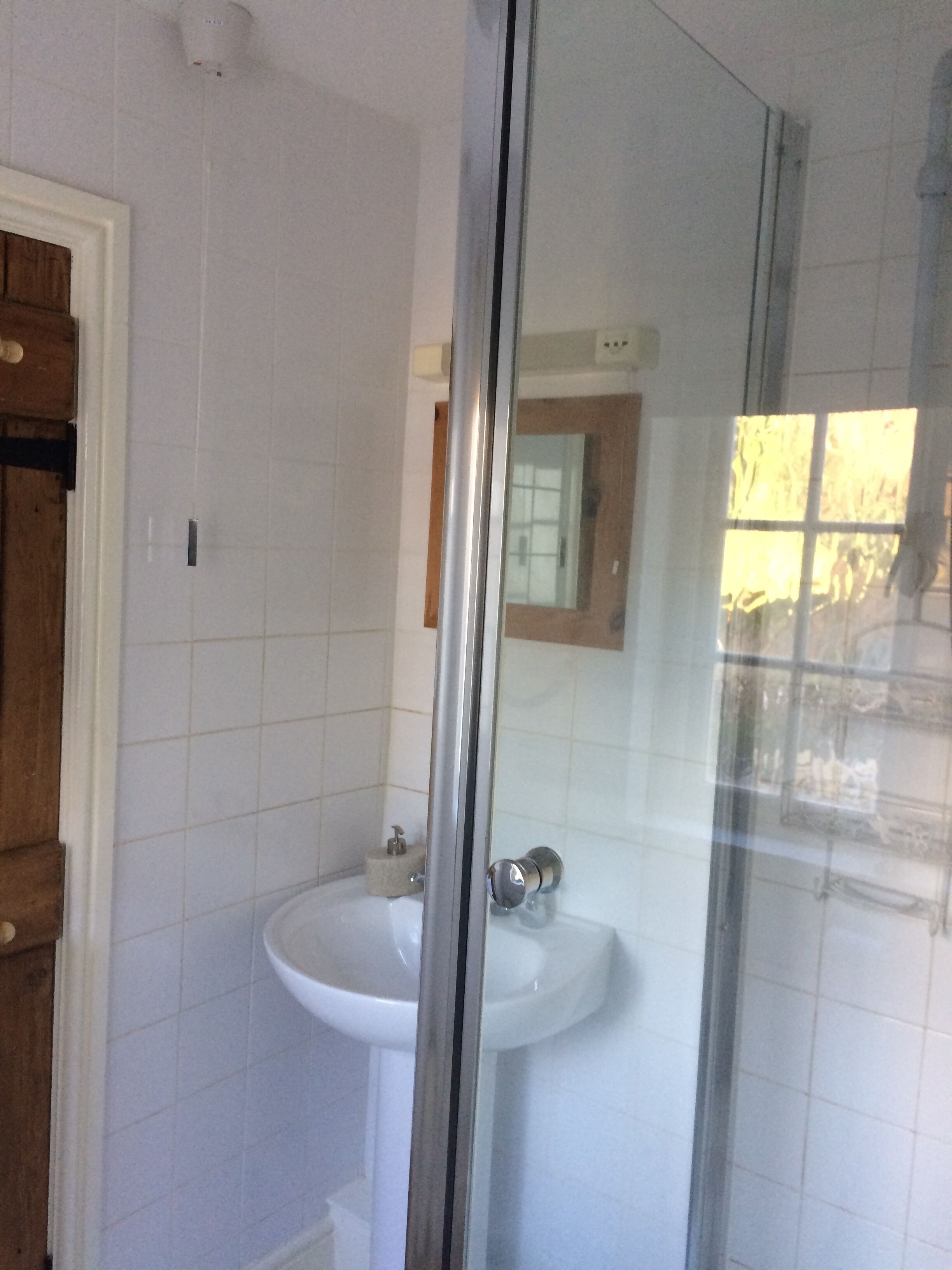 Un baño con cabina de ducha de vidrio, un lavabo blanco y una puerta de madera.