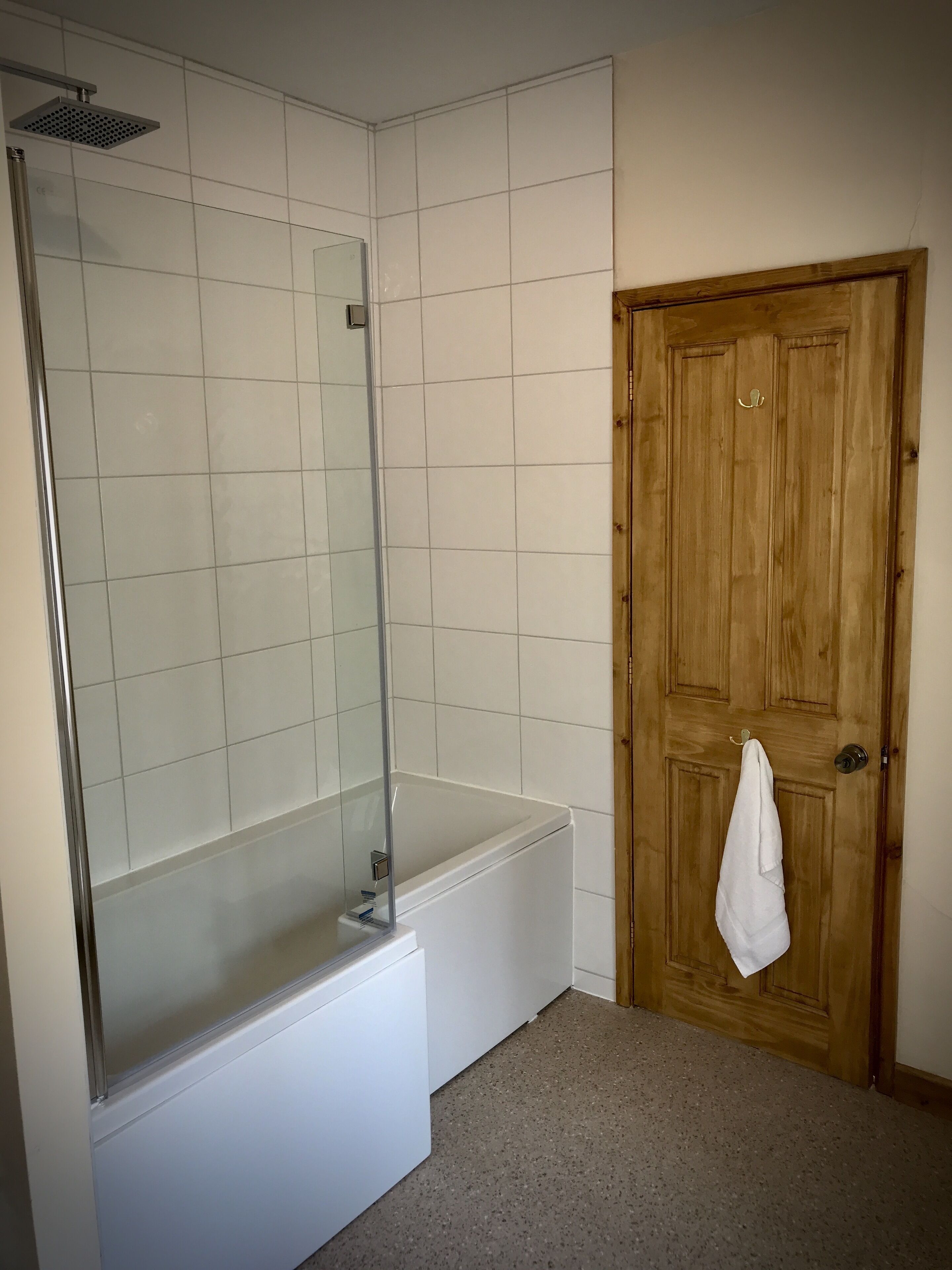 Un baño con ducha de vidrio, bañera blanca y puerta de madera con una toalla colgada.