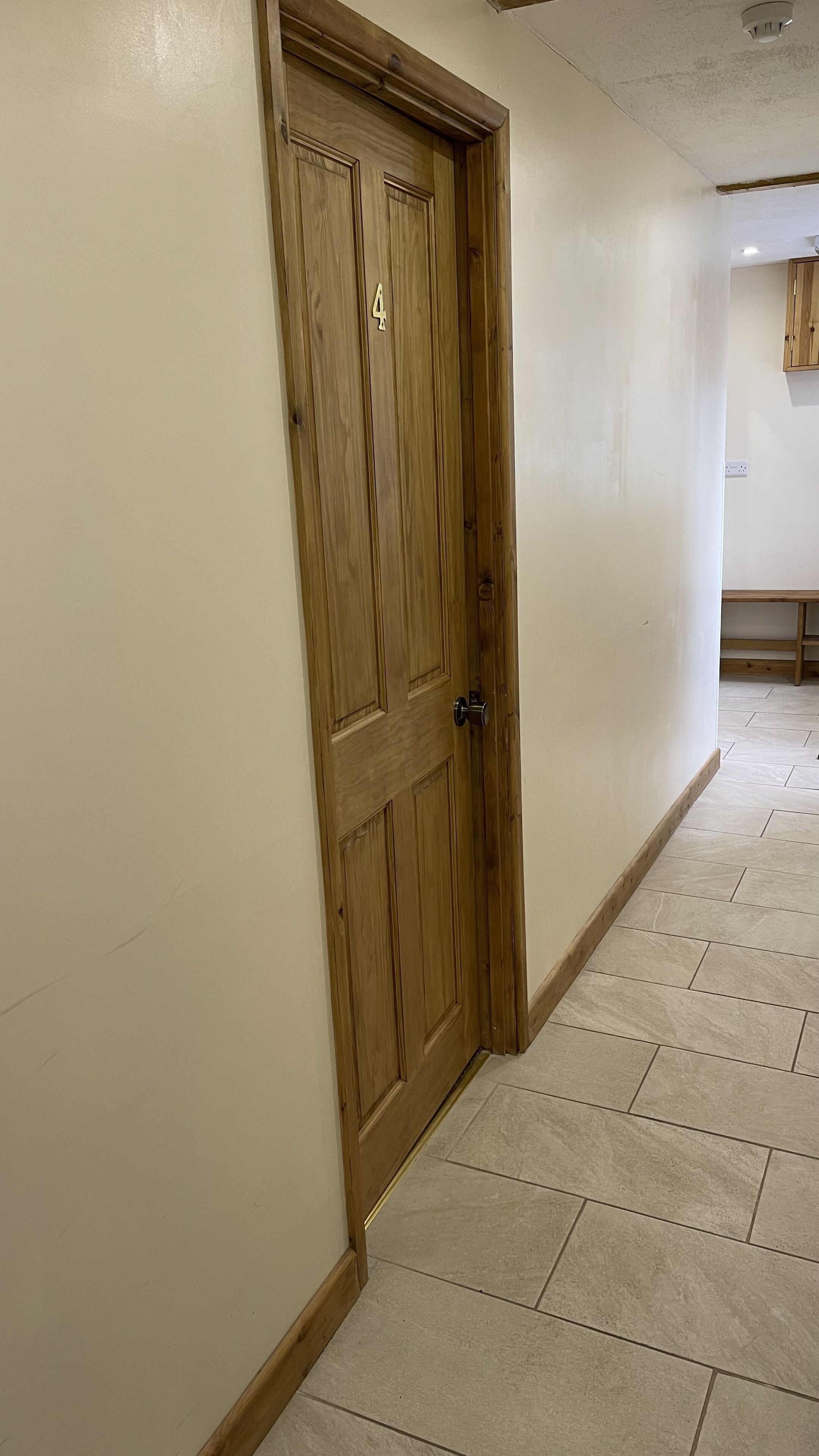 Un couloir avec une porte en bois, des murs de couleur beige et un sol carrelé.
