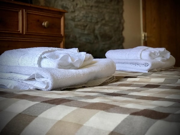 Una cama con un edredón de cuadros y dos toallas blancas dobladas con cuidado.