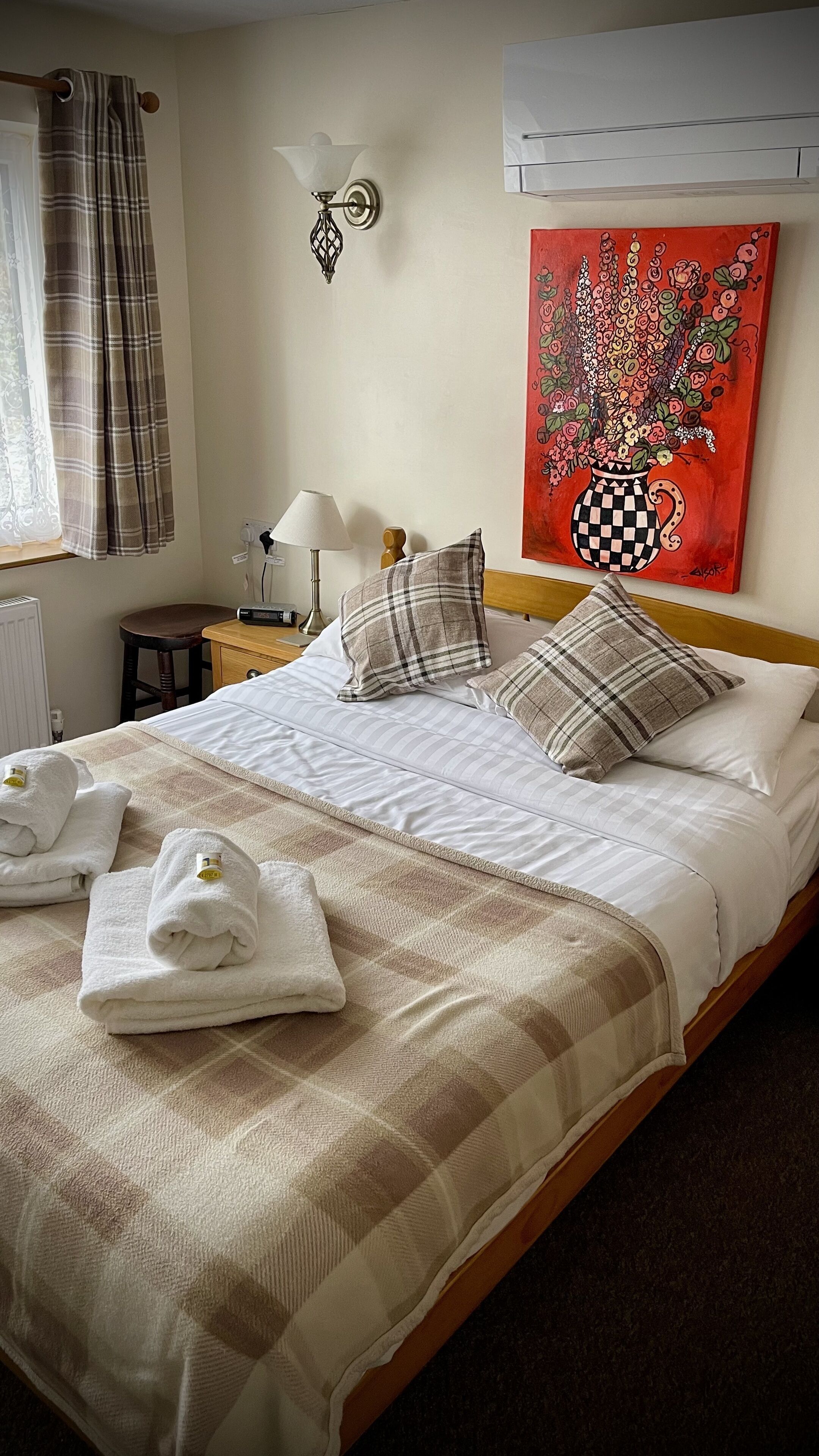 A neatly made bed with a checkered blanket, pillows, and folded towels.