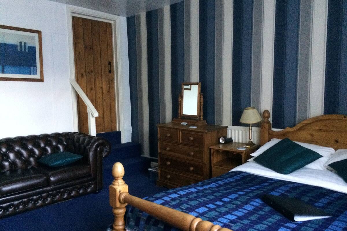 A bedroom with a wooden bed, a dresser, a mirror, a lamp, and a leather armchair.