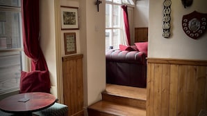 Un cuarto acogedor con paneles de madera, una cortina roja, un cuadro enmarcado, una mesita y una escalera que conduce a una cama con almohadas rojas.
