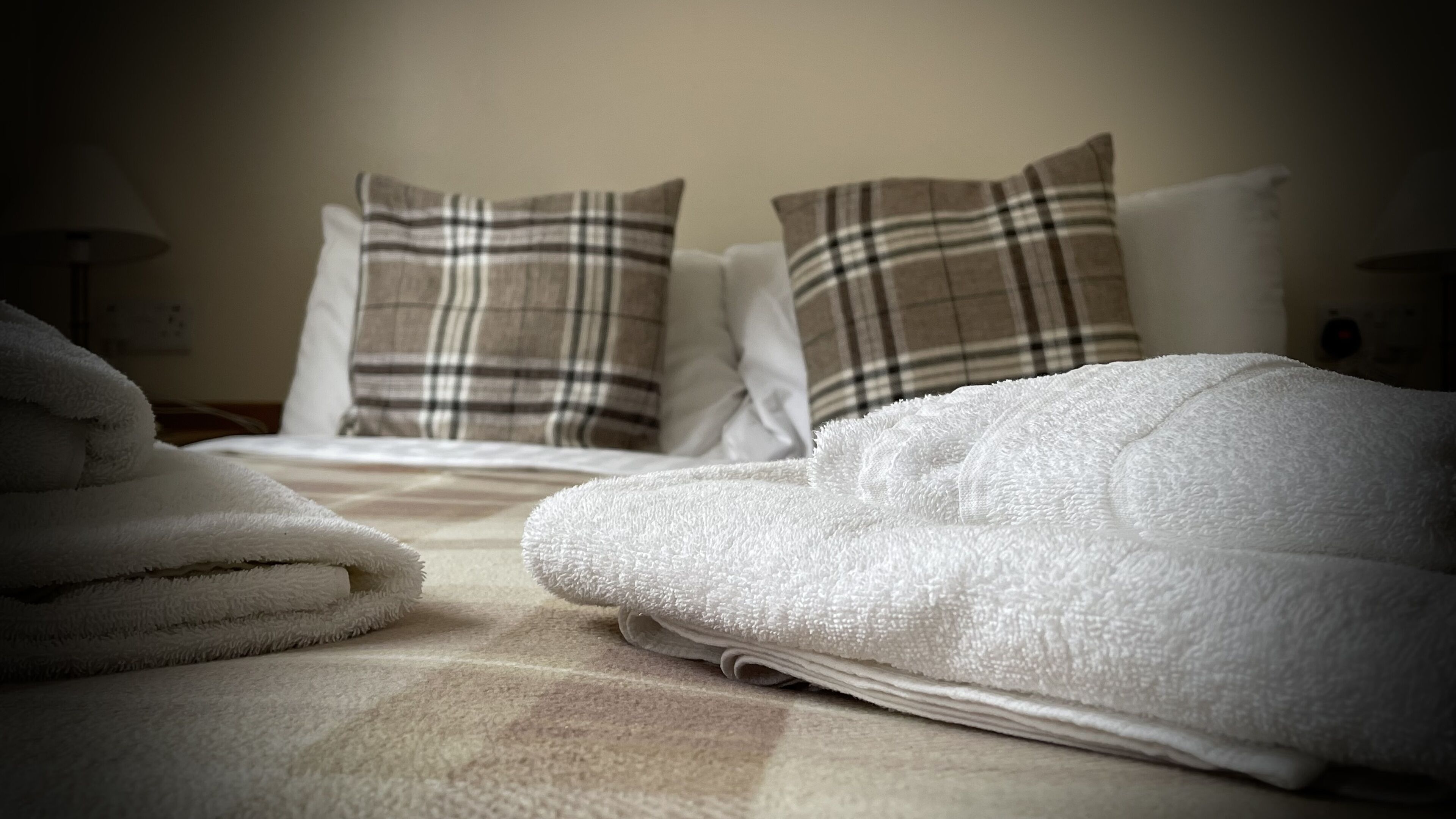 A neatly made bed with white linens and two plaid pillows.