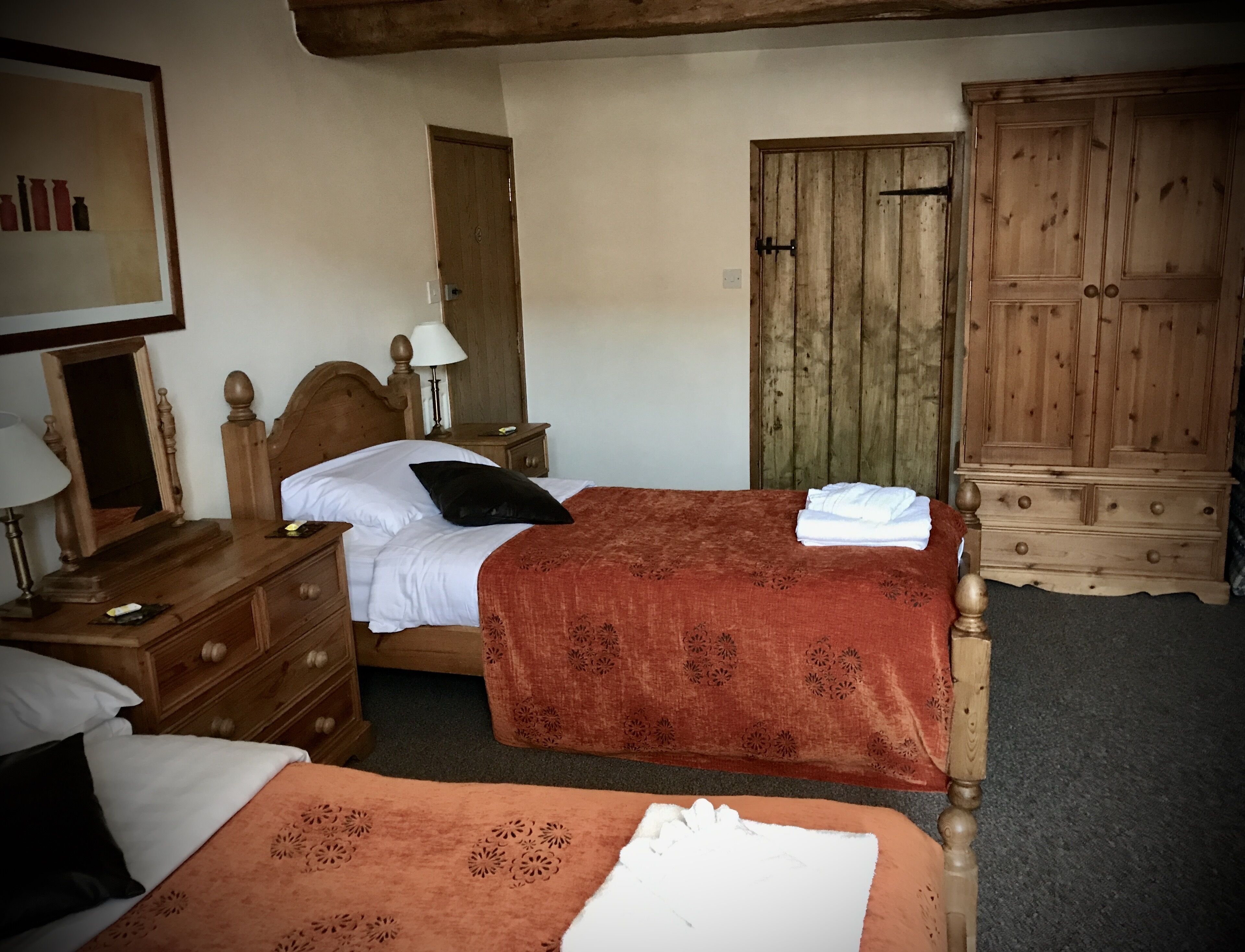 A hotel room with two beds, wooden furniture, a wardrobe, and a mirror.