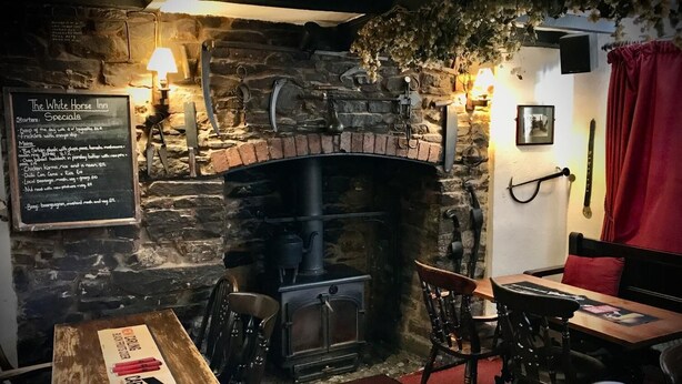 Un acogedor hostal con chimenea de piedra, muebles de madera y un cartel con las especialidades del día.
