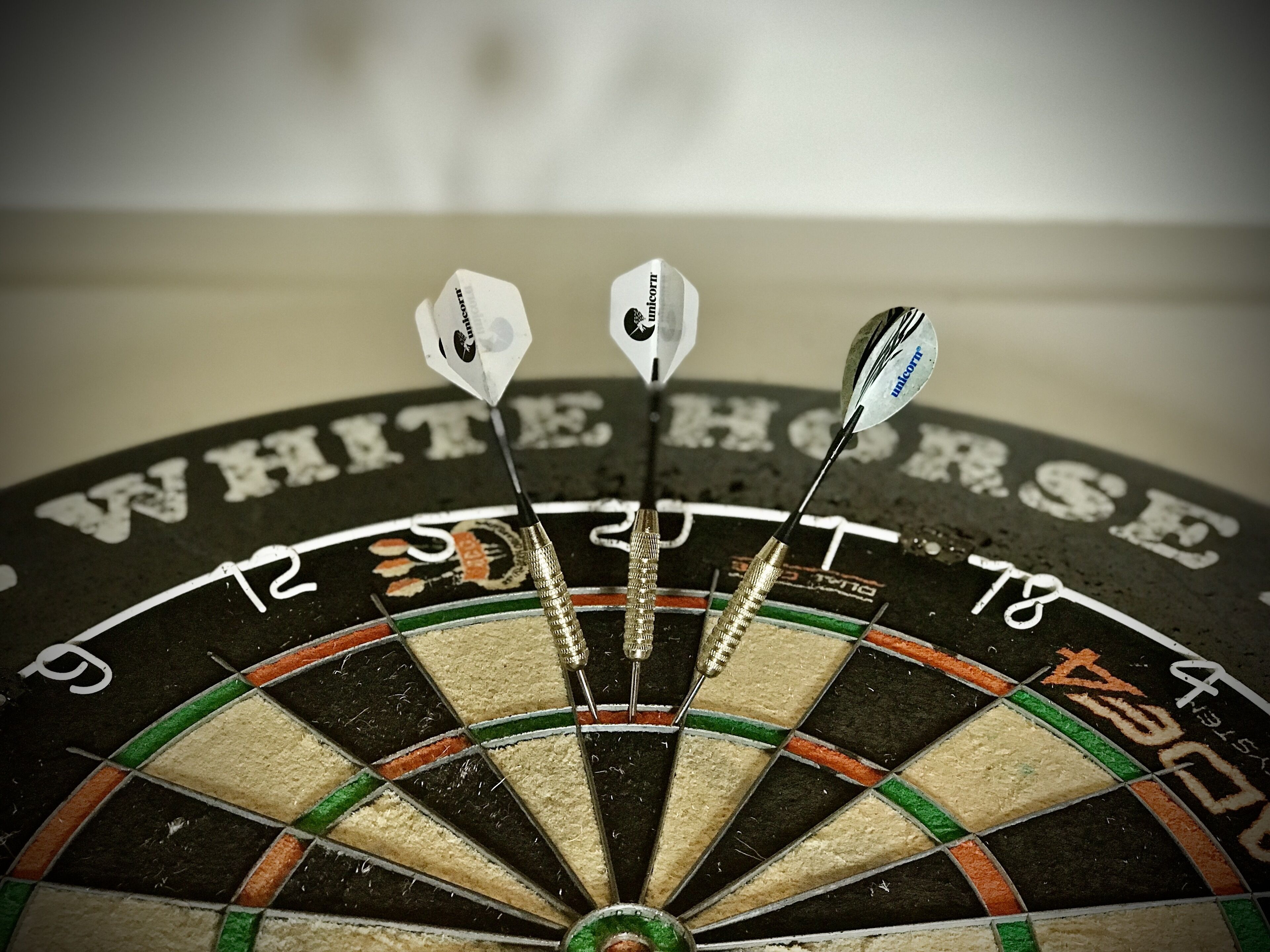 A dartboard with three darts stuck in it, and the words "WHITE HORSE" visible on the board.