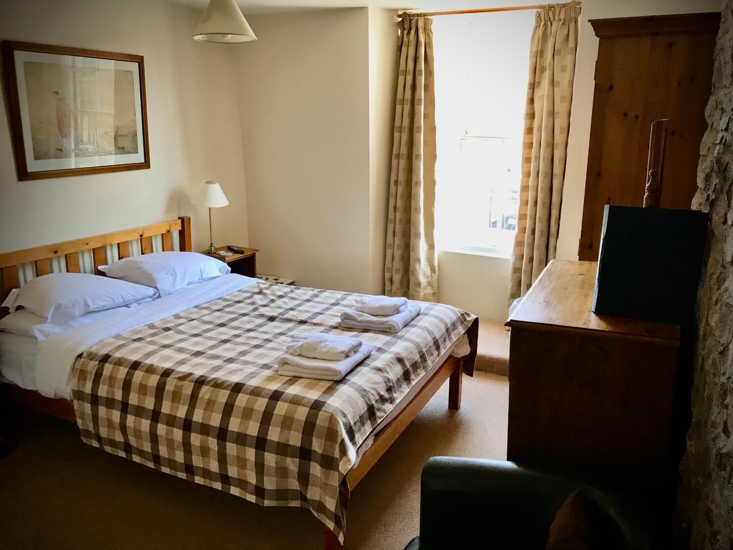 Quarto de hotel com uma cama, uma escrivaninha, uma luminária e um quadro na parede.