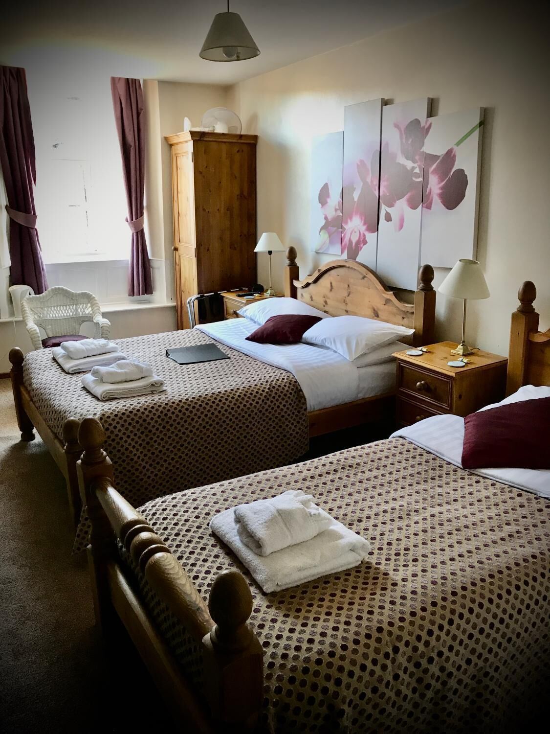 Habitación de hotel con dos camas, un armario de madera, una silla, una mesita de noche y un cuadro en la pared.
