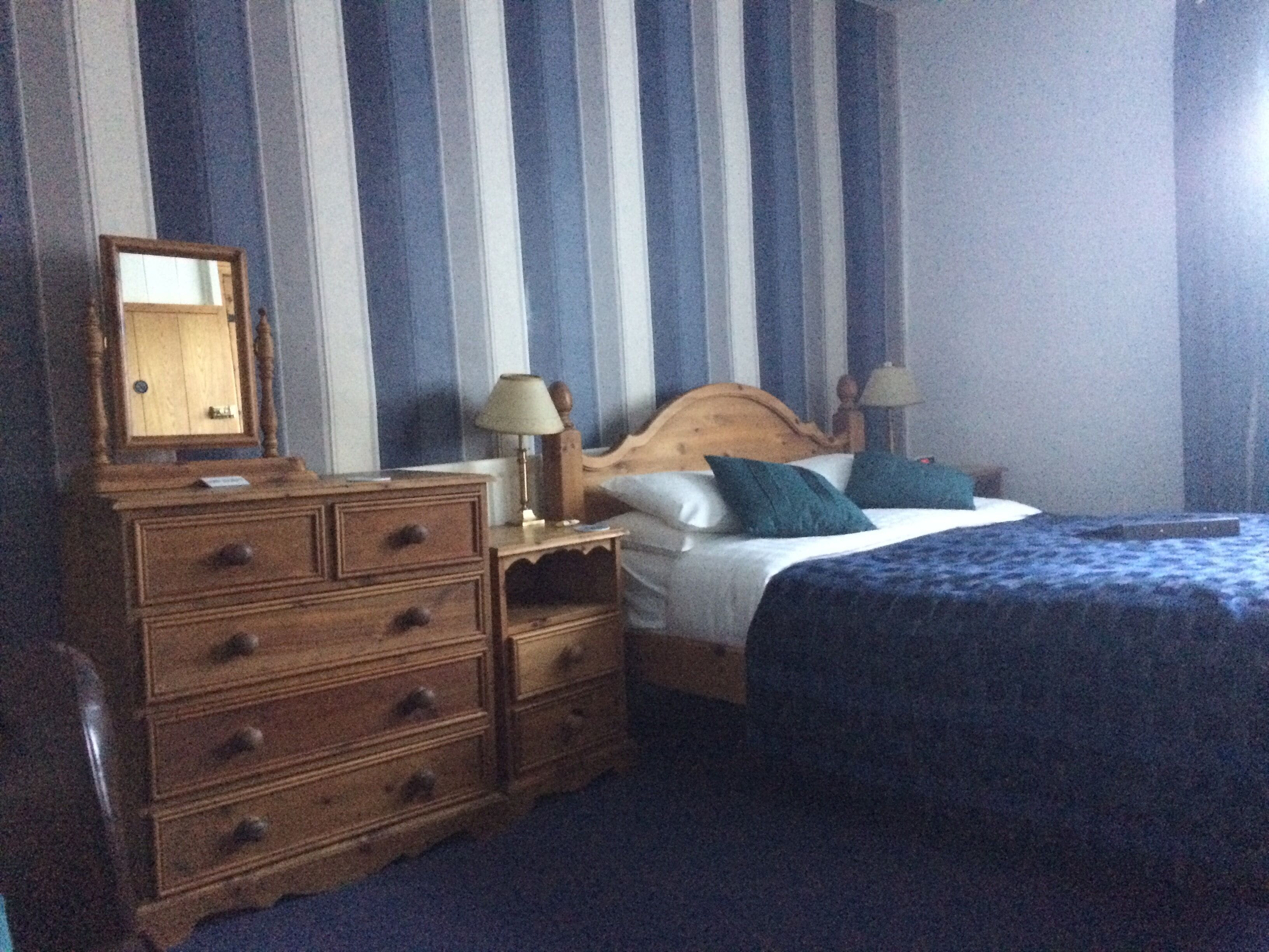 Una camera d'albergo con un comò in legno, un letto con copriletto blu e tende a righe.