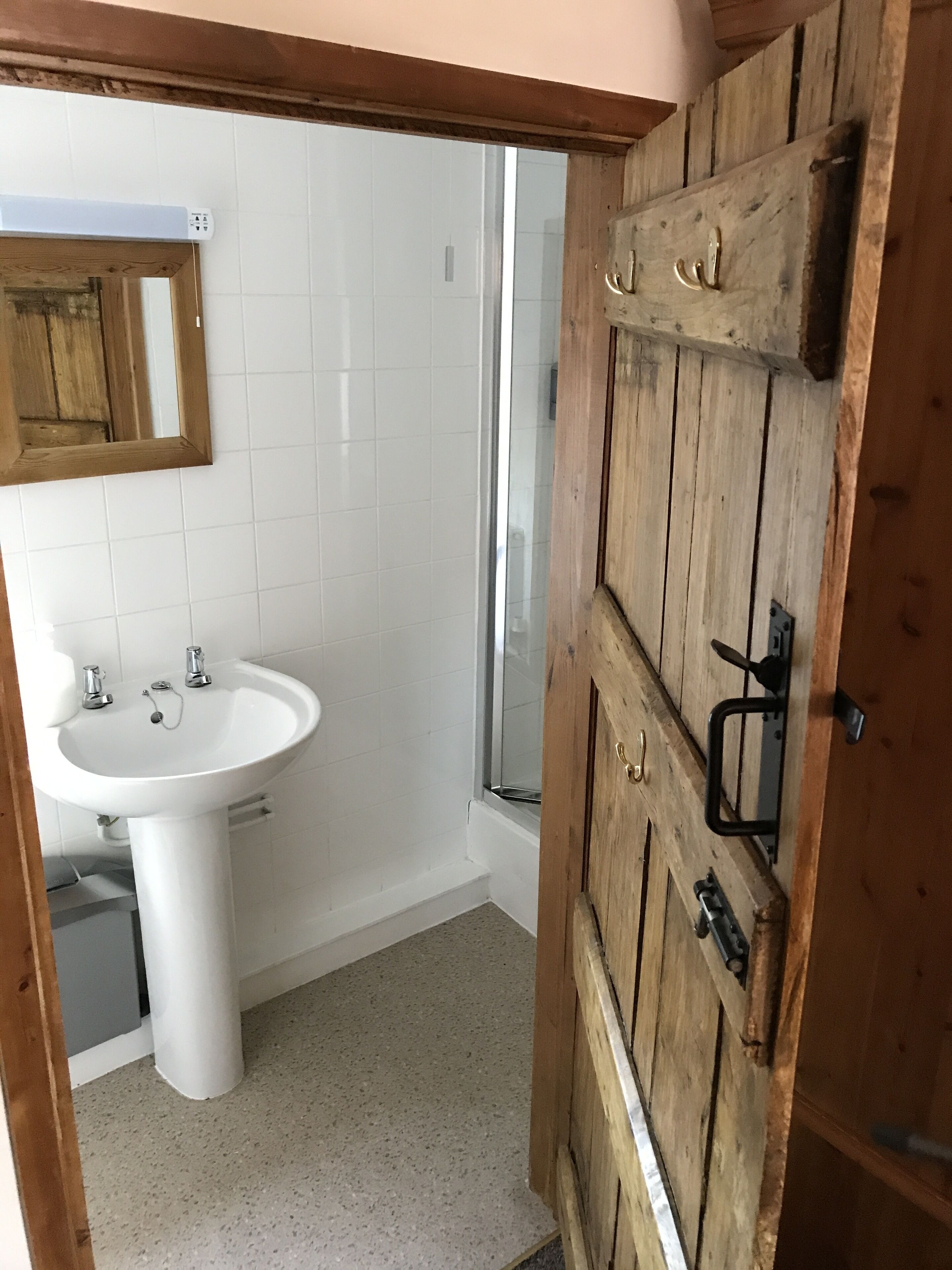Une salle de bain avec un lavabo blanc, une porte en bois et un miroir.