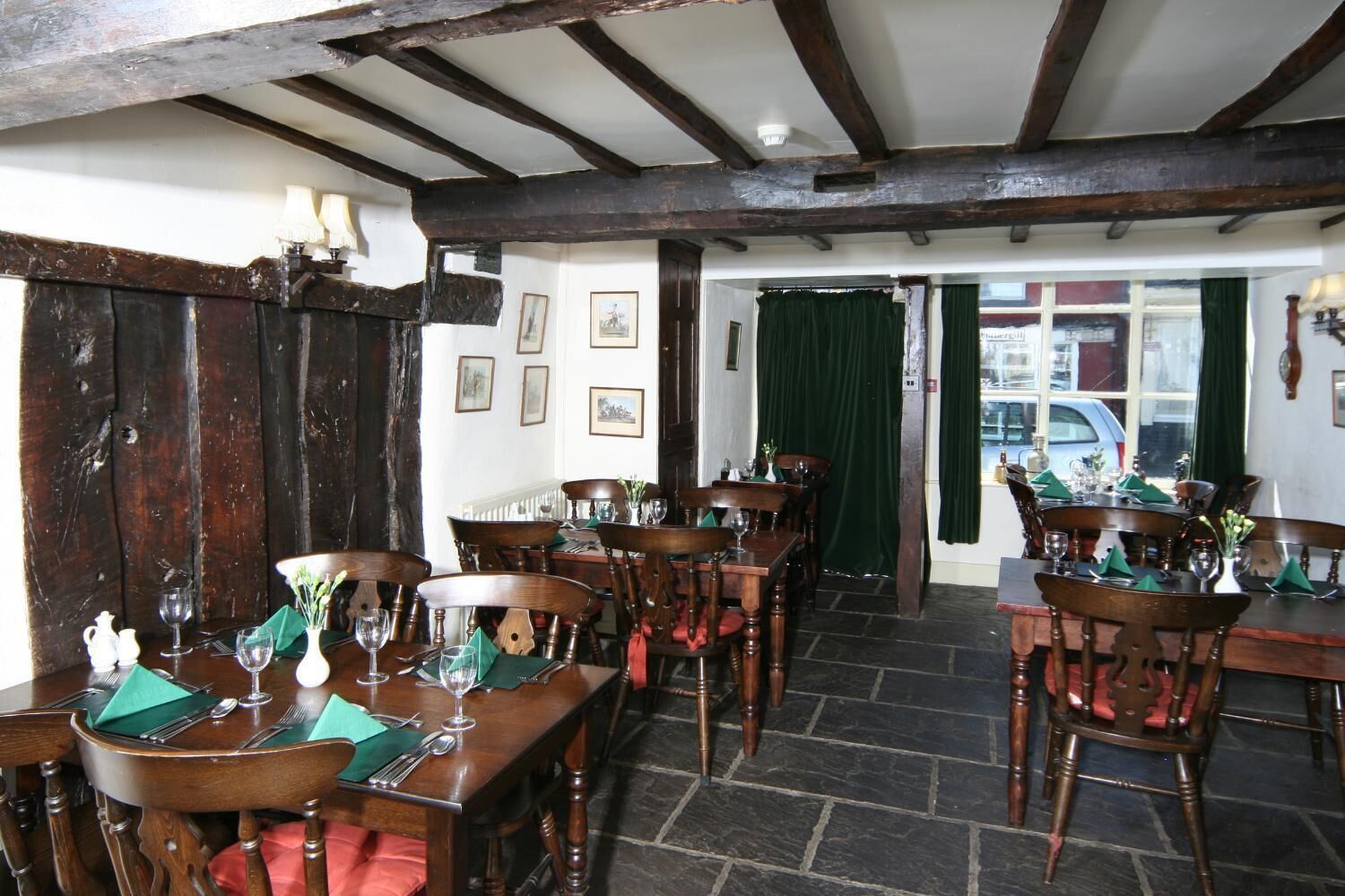 A traditional inn with wooden beams and stone flooring, featuring multiple dining tables set for guests.