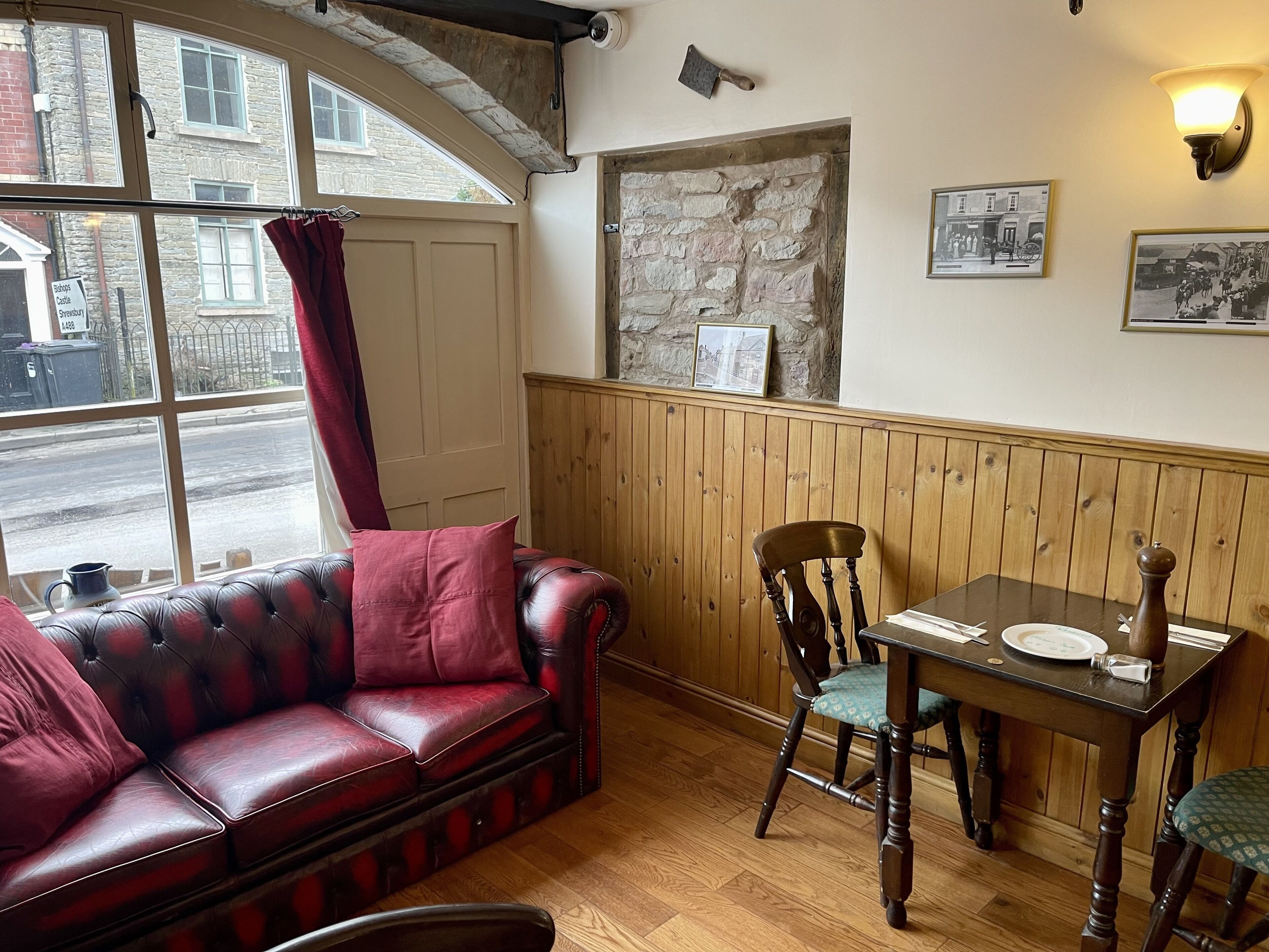 A cozy room with a leather sofa, wooden dining table, and chairs. A stone wall and wooden paneling are visible.