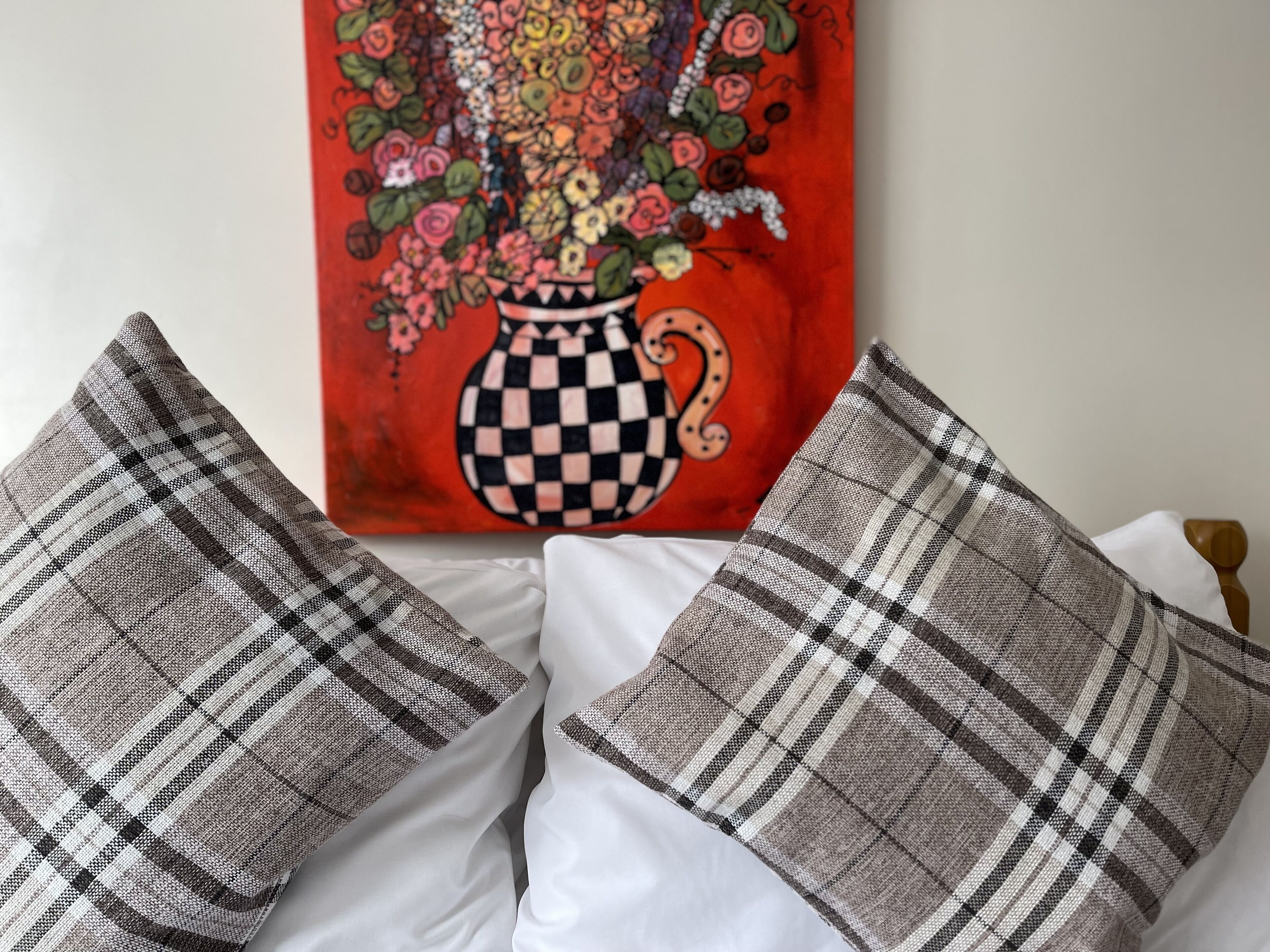 A bed with two pillows and a painting of a vase with flowers.