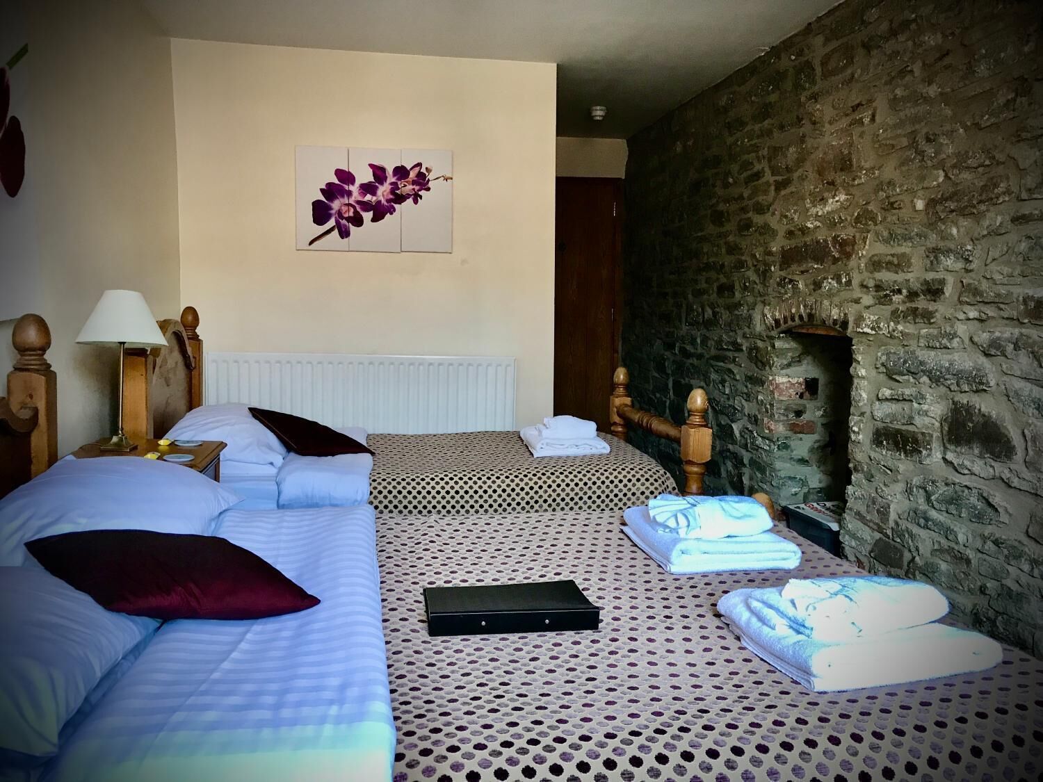 Een hotelkamer met twee bedden, een stenen muur, een radiator, een lamp en een bloemen schilderij.