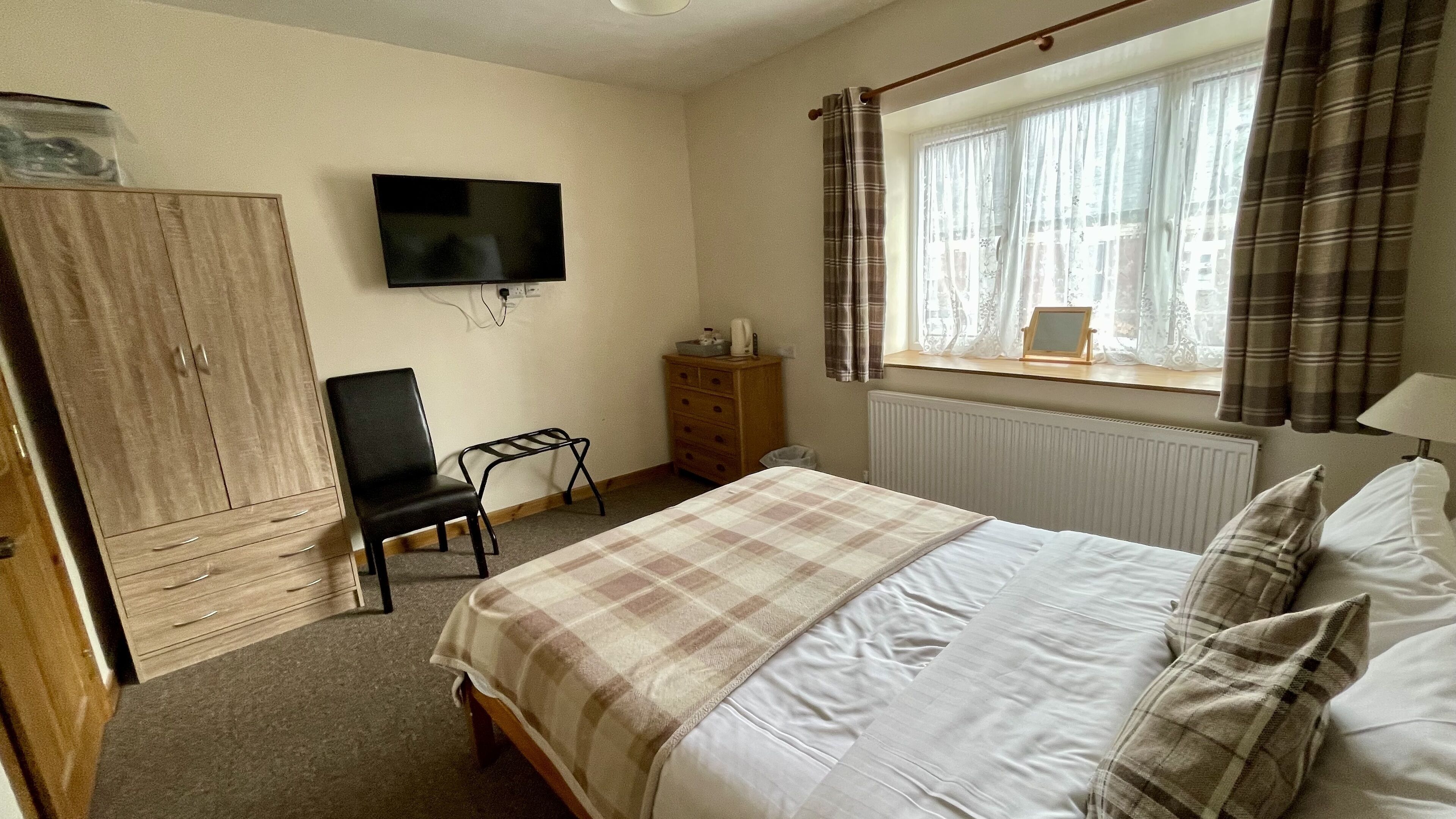 Een slaapkamer met een bed, een stoel, een kledingkast, een televisie en een raam met gordijnen.