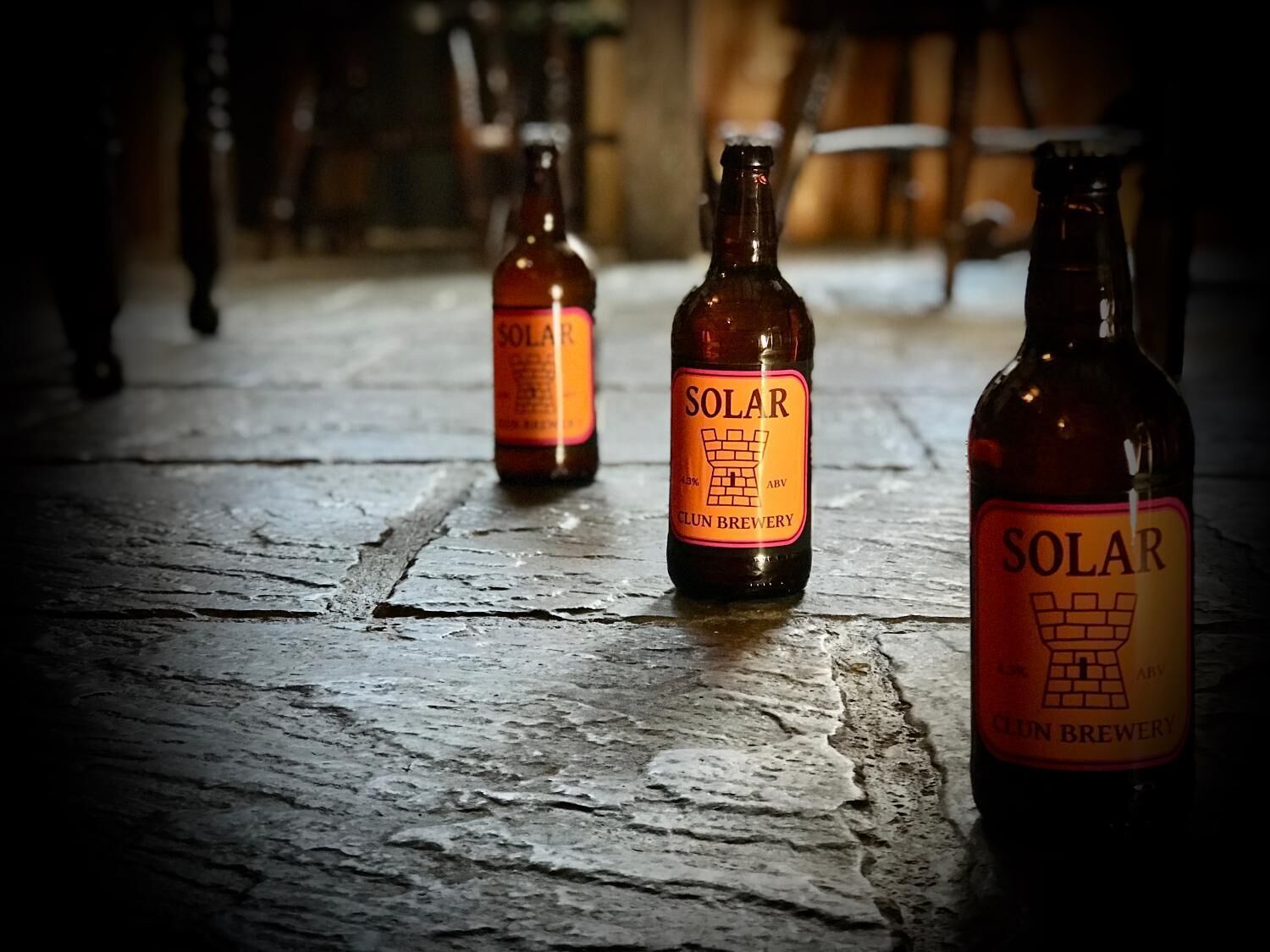 Three bottles of beer with labels reading "SOLAR CLUN BREWERY" on a wooden surface.