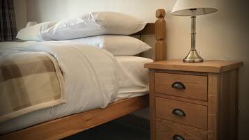 A bed with white linens and a wooden headboard, a bedside table with a lamp, and a checkered throw blanket.