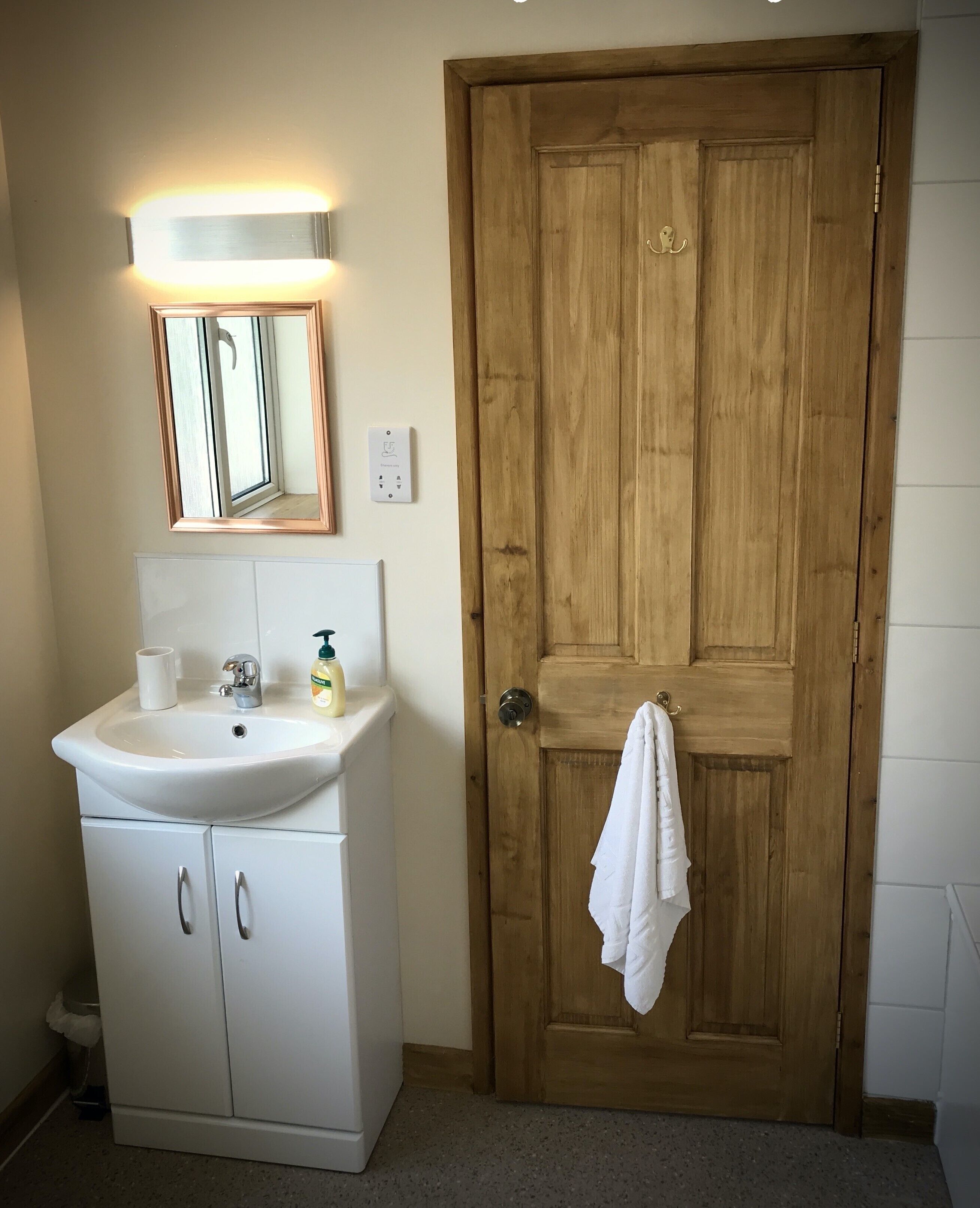 Un baño con lavamanos blanco, espejo y puerta de madera.