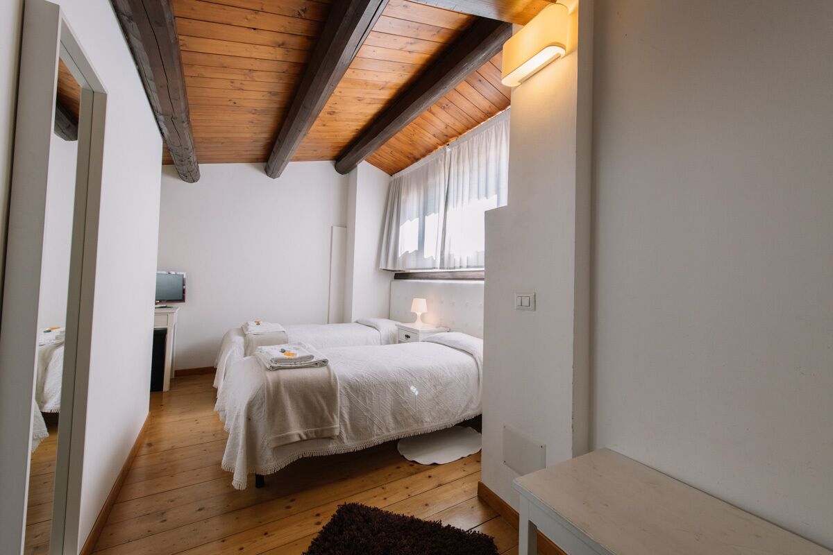 Ein kleines, gemütliches Schlafzimmer mit zwei Betten, einer Holzbalkendecke und einem Fenster mit Vorhängen.