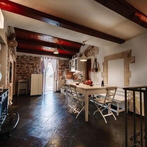 A rustic kitchen with a stone wall, wooden beams, and a dining area with a table and chairs. - La Casa di Matilde (Ragusa)