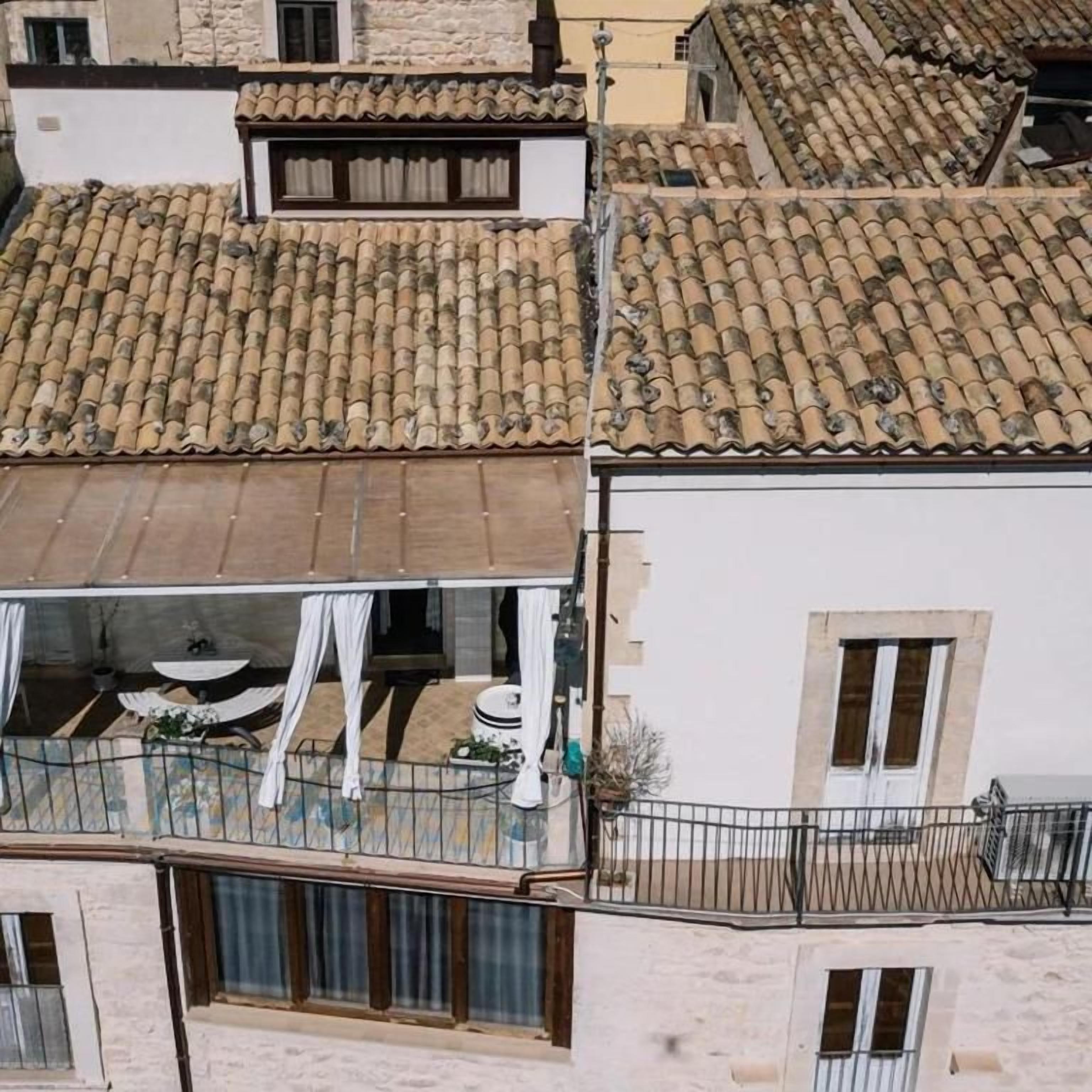 Un immeuble d’habitation avec un toit recouvert de tuiles, des balcons dotés de garde-corps et une fenêtre avec des rideaux.