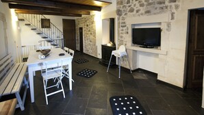 A modern kitchen with a dining area, stone walls, a fireplace, and a TV mounted on the wall. - La Casa di Matilde (Ragusa)