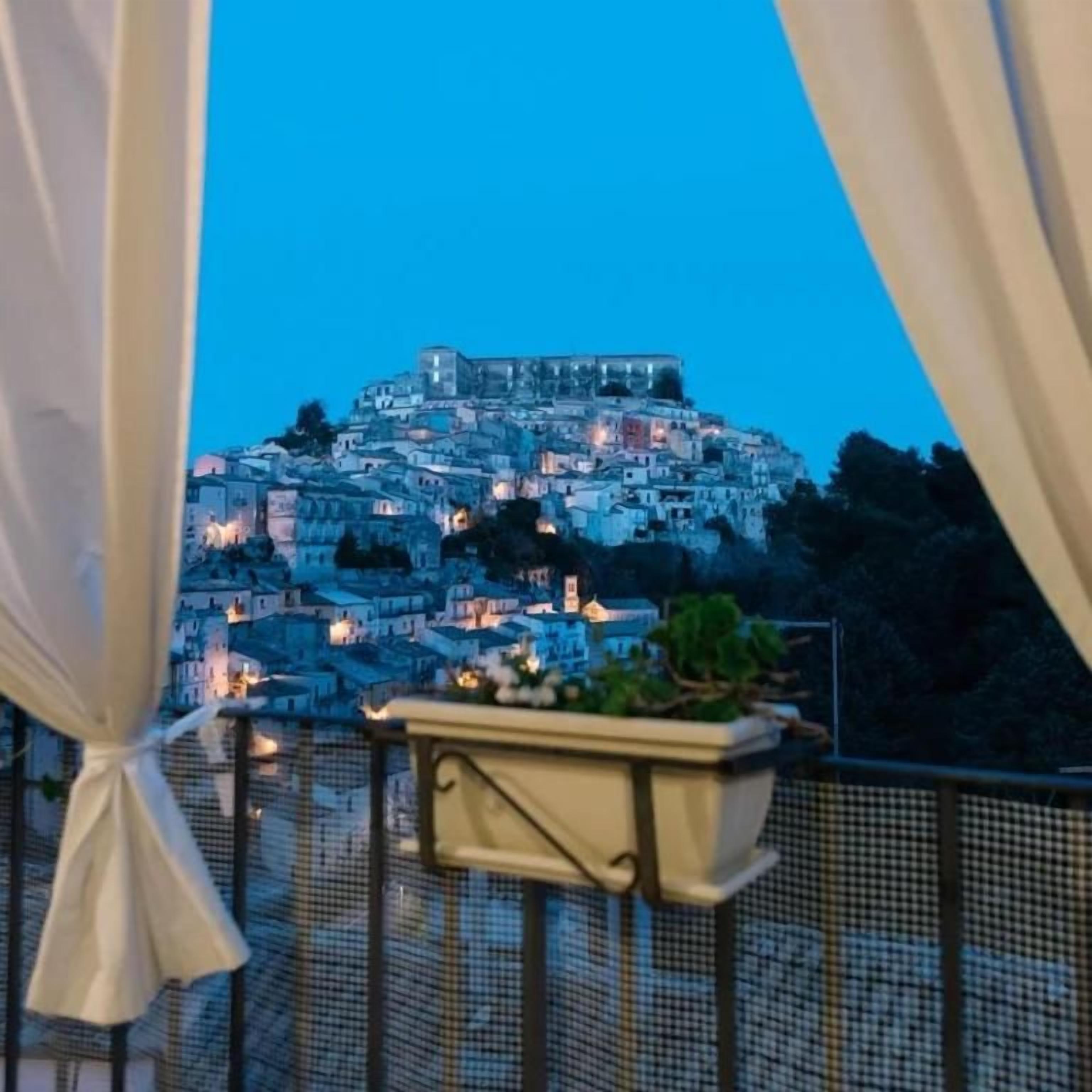 Ein Balkon mit Blick auf eine dicht bebauten Hügelstadt in der Abenddämmerung.