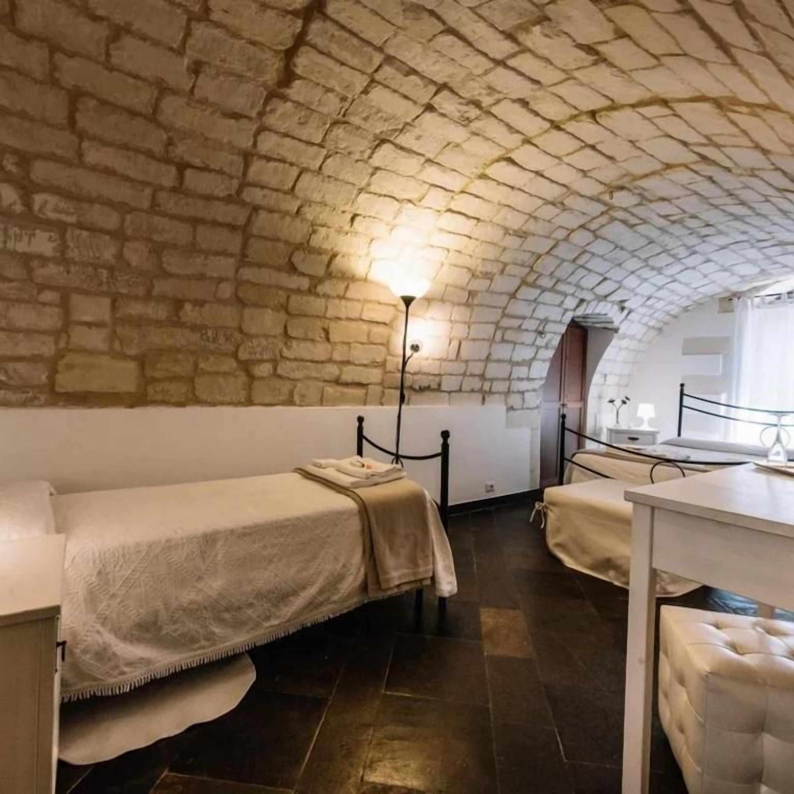Une pièce dotée d’un plafond voûté en briques, d’un lit, d’une table de chevet et d’une petite table avec une lampe.