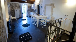 A rustic kitchen with stone walls, a wooden ceiling, and a dining area with white chairs and a table. - La Casa di Matilde (Ragusa)
