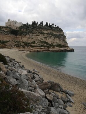 A coastal landscape with a sandy beach, rocky outcrops, and a building on a cliff. - Casa Calieri (Tropea)