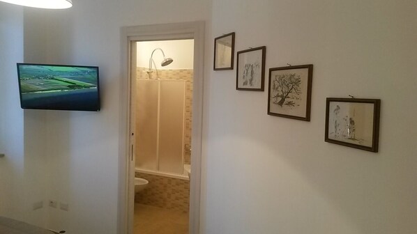 A hallway with a mounted TV, a shower area, and framed artwork on the wall. - Casa Calieri (Tropea)
