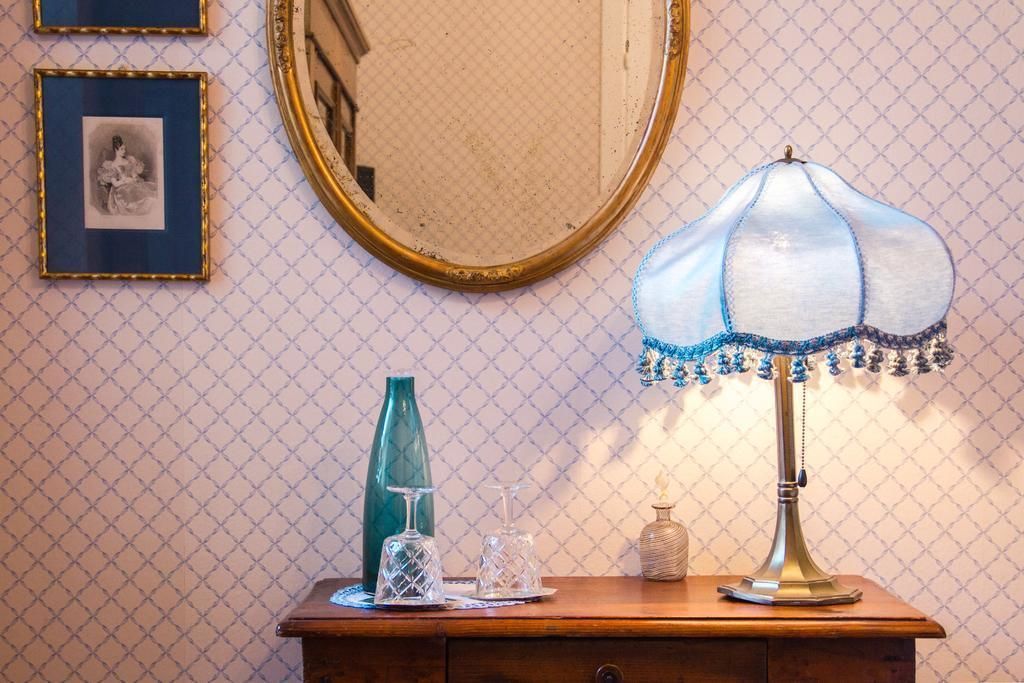 A wooden dresser with a mirror, a lamp, and framed pictures on a patterned wall.