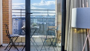 A balcony with a view of the city, a table with a potted plant, and two chairs. - Deluxe Kensington Apartment With Balcony (London)