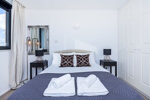 A neatly made bed with two rolled towels, a large mirror, and two bedside tables with lamps. - Deluxe Kensington Apartment With Balcony (London)