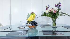 A glass table with a fruit bowl, a vase with flowers, and a clear glass. - Deluxe Kensington Apartment With Balcony (London)