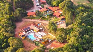 Vue aérienne d’un complexe hôtelier comprenant plusieurs bâtiments, une piscine et une végétation luxuriante environnante.