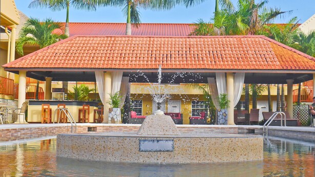 A pool area with a fountain, surrounded by palm trees and a covered seating area. - Hotel North Resort (Paramaribo)
