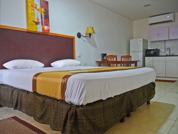 A hotel room with a large bed, a desk with two chairs, a kitchen area, and a wall-mounted lamp. - Hotel North Resort (Paramaribo)