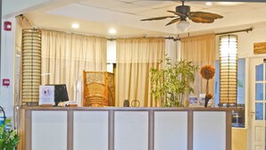 A reception desk with a ceiling fan, a sign indicating a smoking area, a potted plant, and a decorative vase. - Hotel North Resort (Paramaribo)