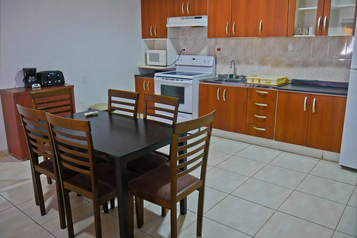 Una cocina compacta con armarios de madera, un microondas, una estufa y una mesa de comedor con sillas.