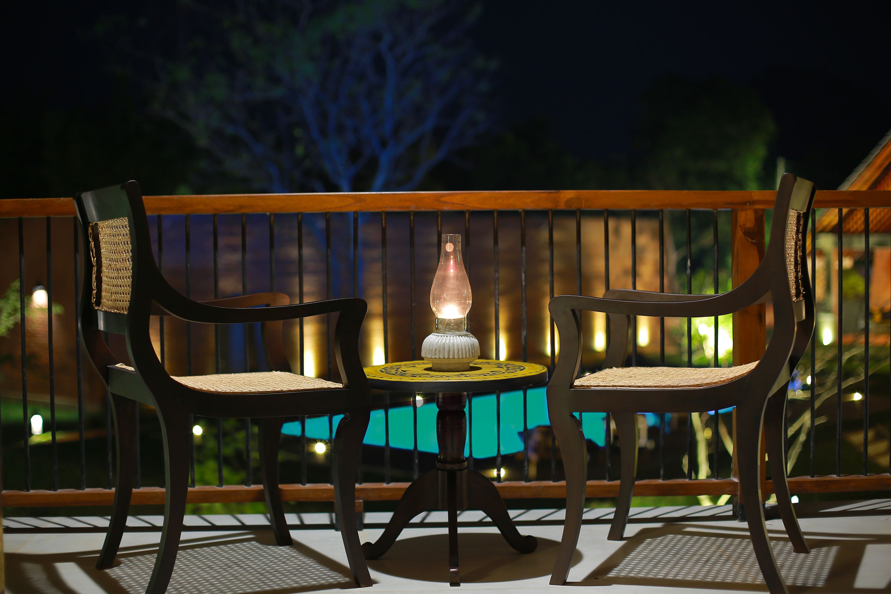 A wooden deck with two chairs and a table, featuring a lit table lamp.