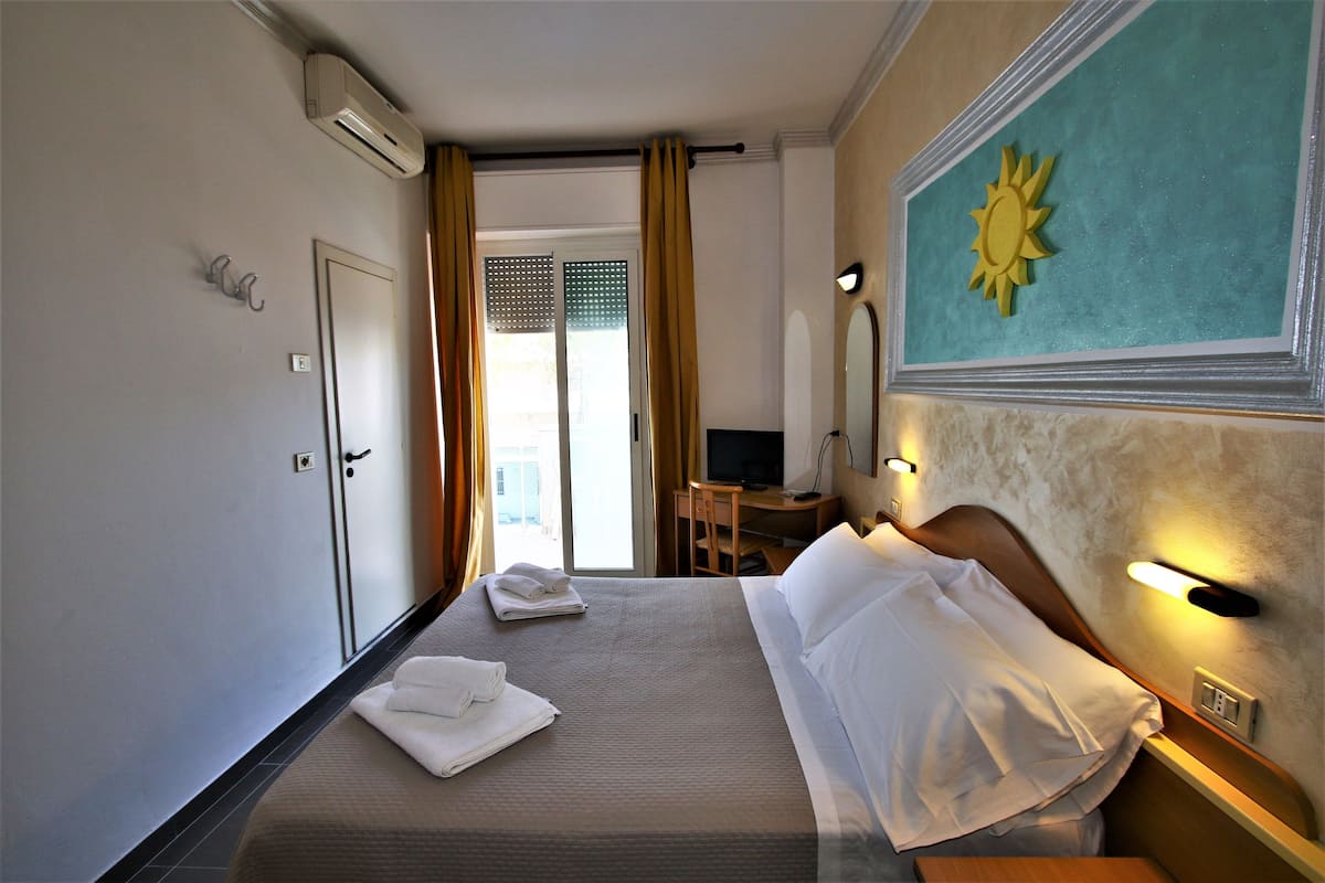 A hotel room with a bed, a desk, a chair, and a TV.