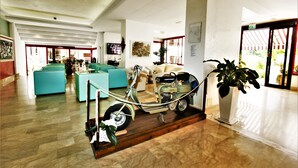 Un hall d’entrée spacieux, agrémenté d’une moto ancienne, de canapés turquoise et d’une grande plante en pot.